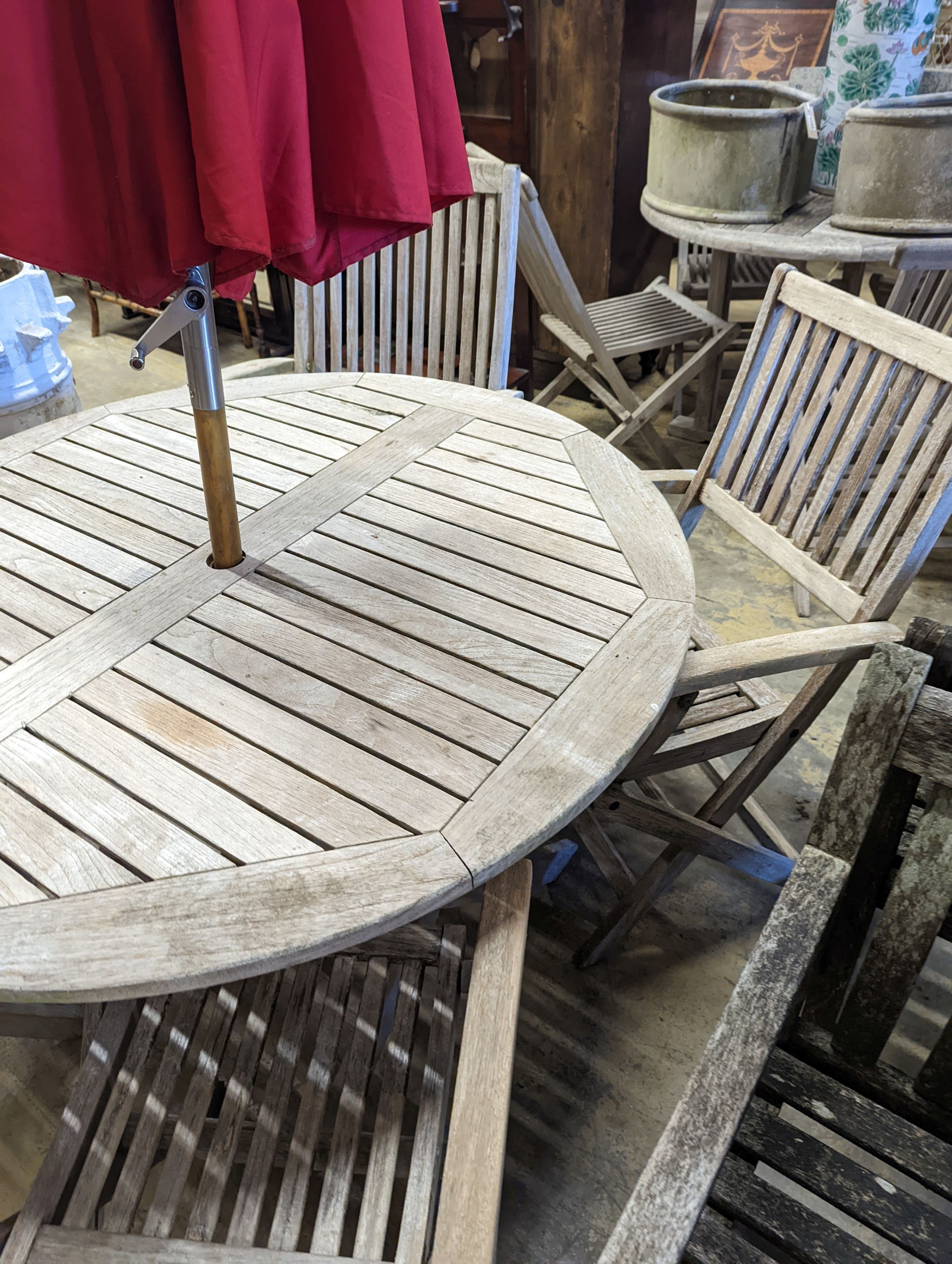 A circular weathered teak folding garden table, diameter 120cm, height 74cm, four folding elbow chairs and a parasol